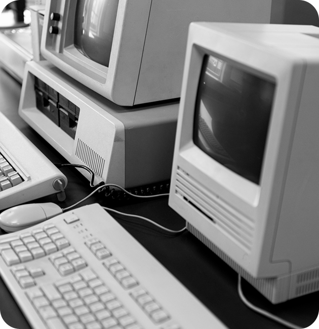 Row of old CRT computers on a long desk; black and white