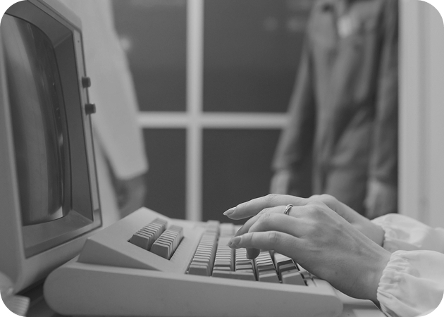 Person typing on an old CRT computer; black and white