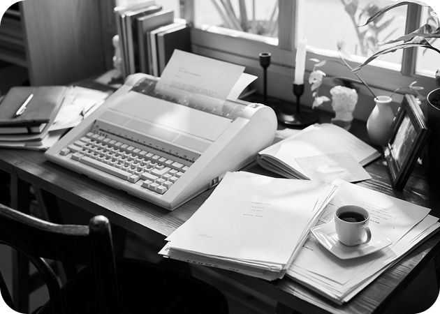 Old typewriter on desk covered in papers and notepads